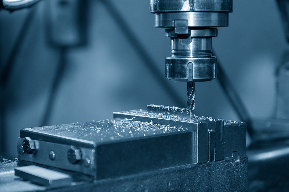 hands holding a piece of metal and machine drilling a hole in it