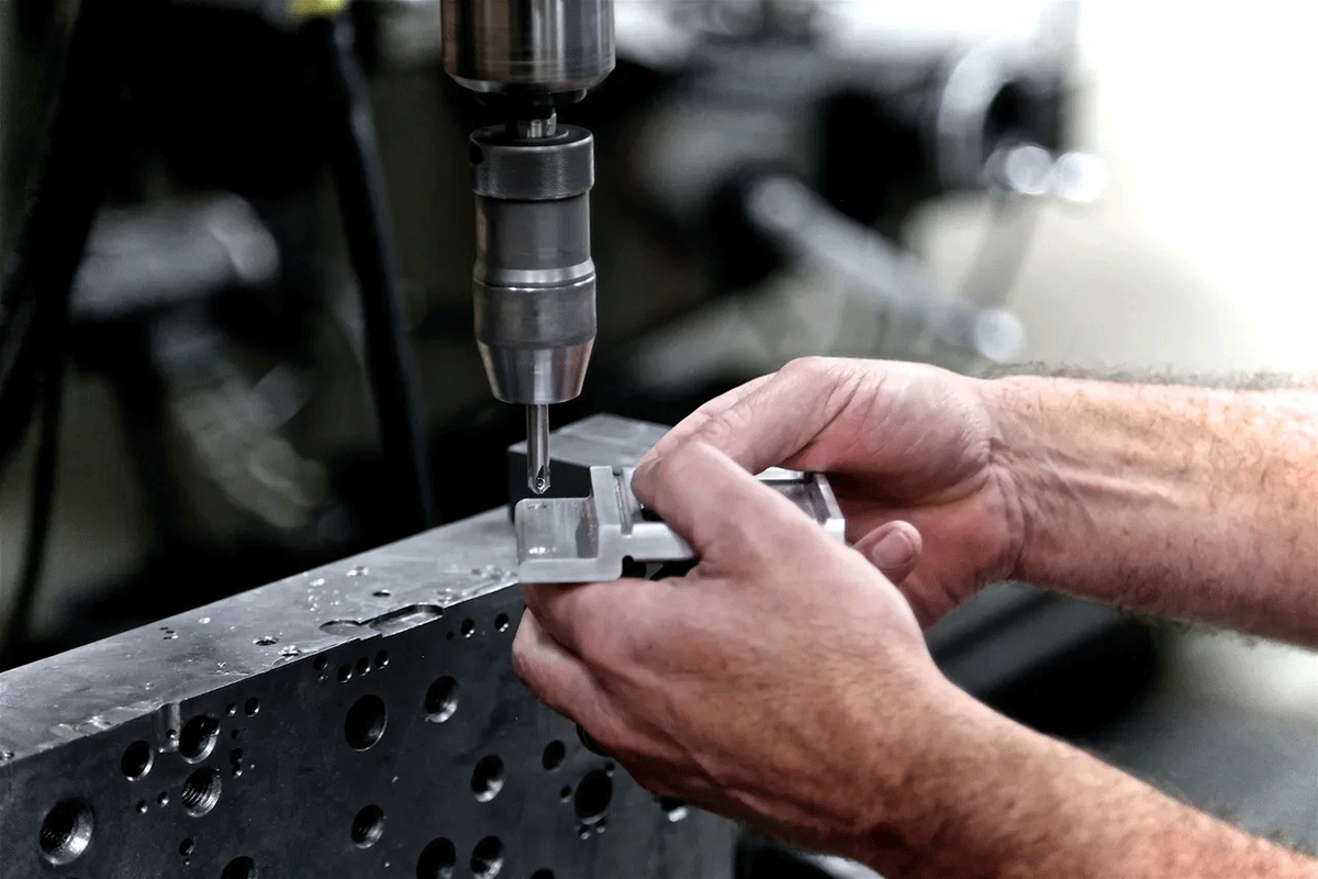 hands holding a piece of metal and machine drilling a hole in it